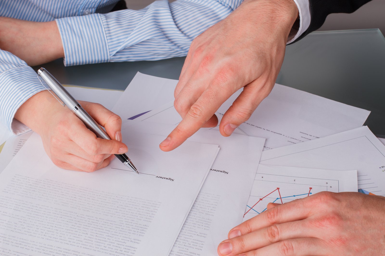 One person pointing to where another should sign a document, with no faces visible