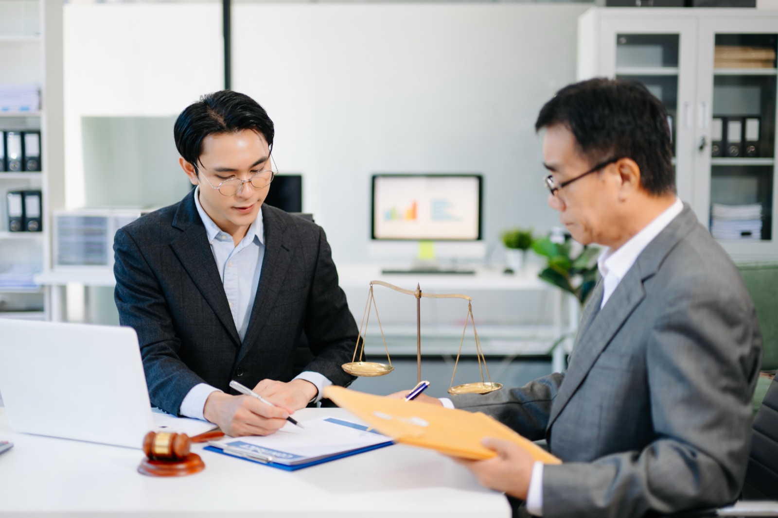 A lawyer advising a business client across a desk, with scales of justice and case documents